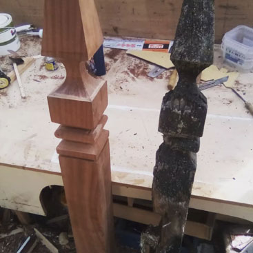 Newly crafted wooden post beside an old, decayed one on a workbench in a woodworking shop