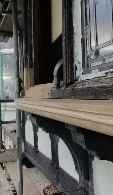 New wooden sill fitted beneath an old leaded window on a timber-framed building during restoration work